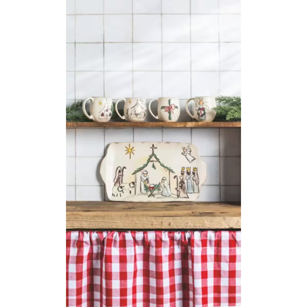 A ceramic Christmas nativity scene serving platter displayed on a wooden shelf in a kitchen setting, with white tiled walls, four decorated mugs on the shelf above, and a red and white gingham checkered curtain below.