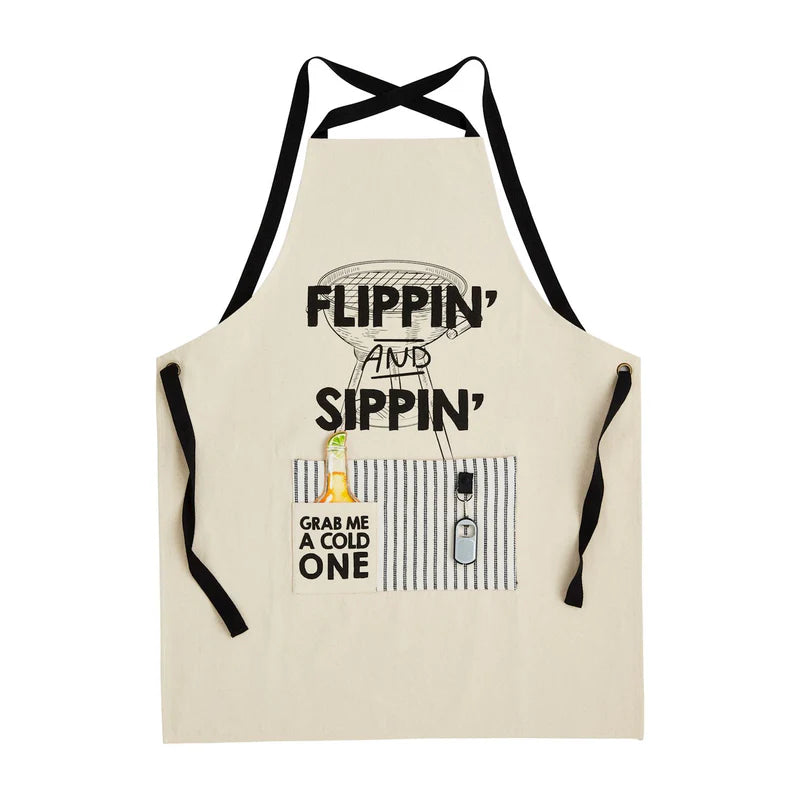 An off-white canvas kitchen & grilling apron with black neck and waist straps, featuring a graphic print of a grill and the text 'FLIPPIN' AND SIPPIN' and 'GRAB ME A COLD ONE' on the front pocket.