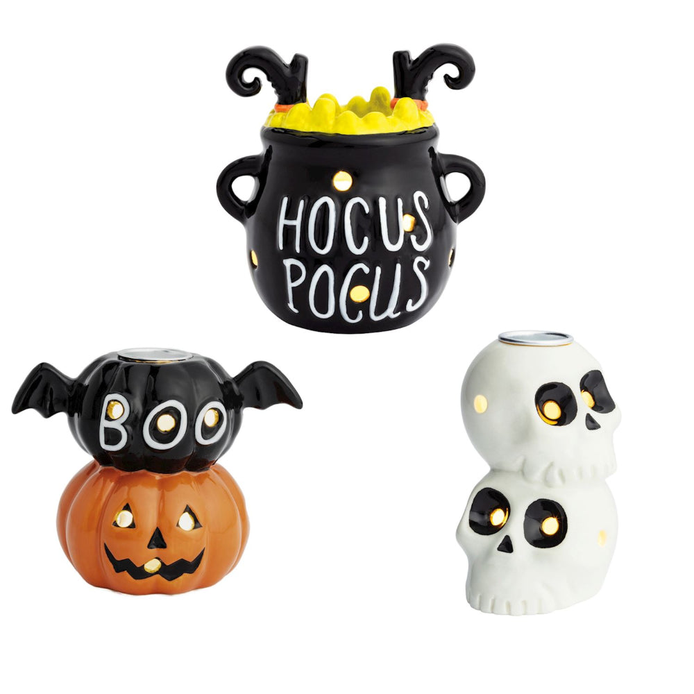 Halloween-themed decorative candle holders including a black cauldron with "Hocus Pocus" , bat, pumpkin, and two stacked skulls on a white background.
