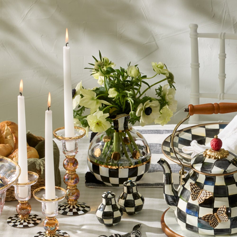 Decorative table setting with checkered teapot, candles, and flowers.