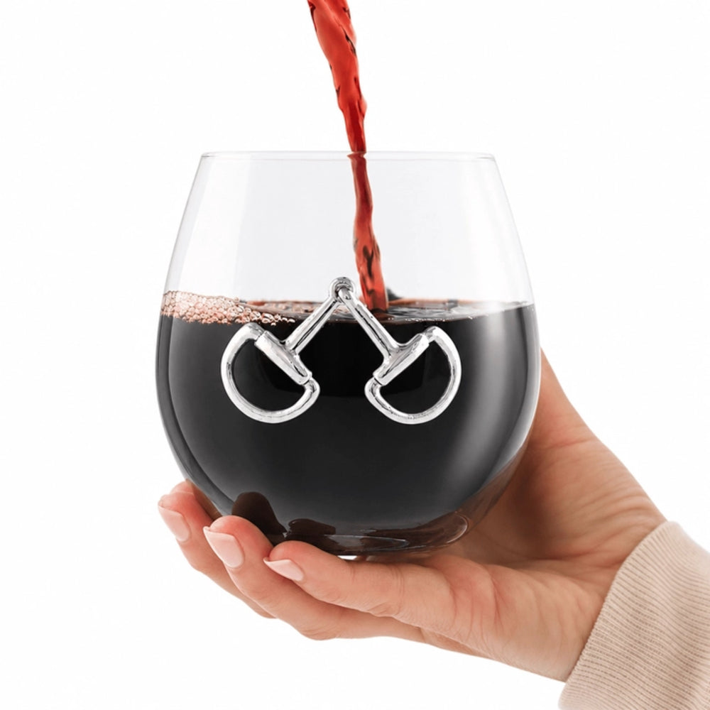 A hand holding a clear stemless wine glass with a silver bicycle handlebar design, with red wine being poured into it, on a white background.