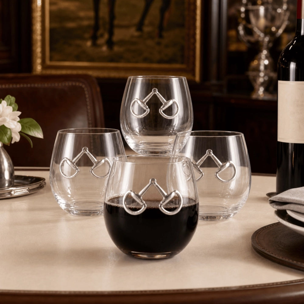 Four clear stemless wine glasses with a silver horse-bit motif, arranged on a dining table with a bottle of red wine and a glass of red wine in the foreground.