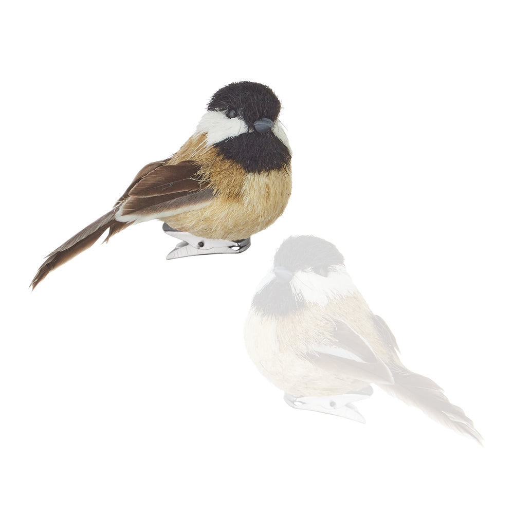 A small bird figurine or ornament shown on a plain white background, with a faint mirrored reflection below it. The bird has a black head, white cheek, warm tan body, brown wings, and a gray beak and feet.