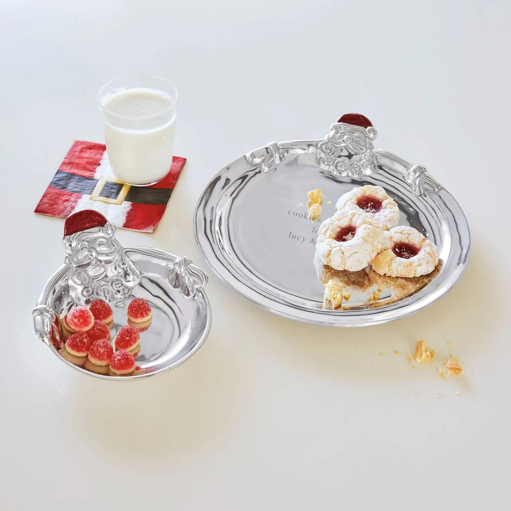 Hugging santa candy dish with santa face and red hat with other holiday entertaining items that have cookies and a santa themed napkin with milk on a white backround.