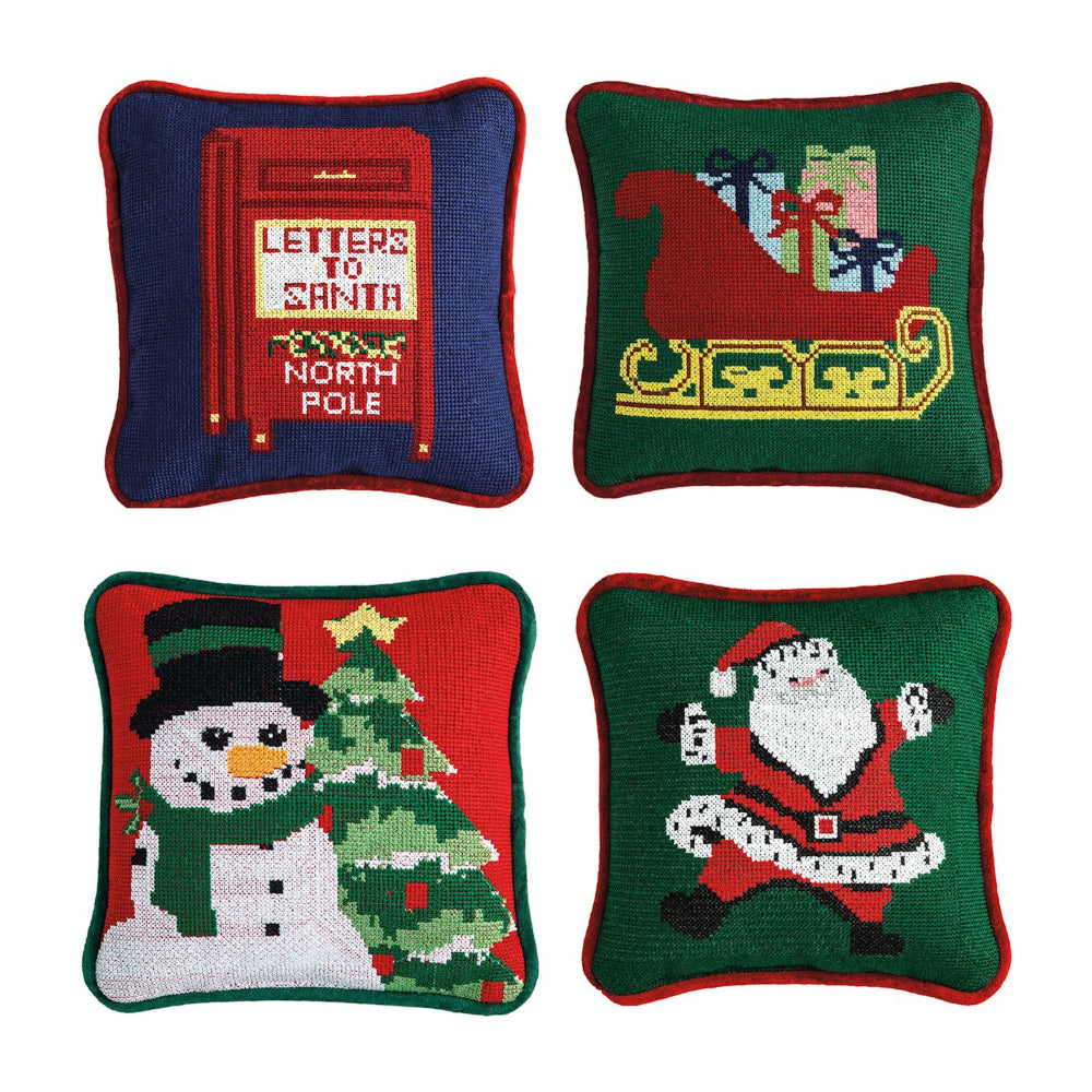 Four Christmas-themed needlepoint pillows on a white background