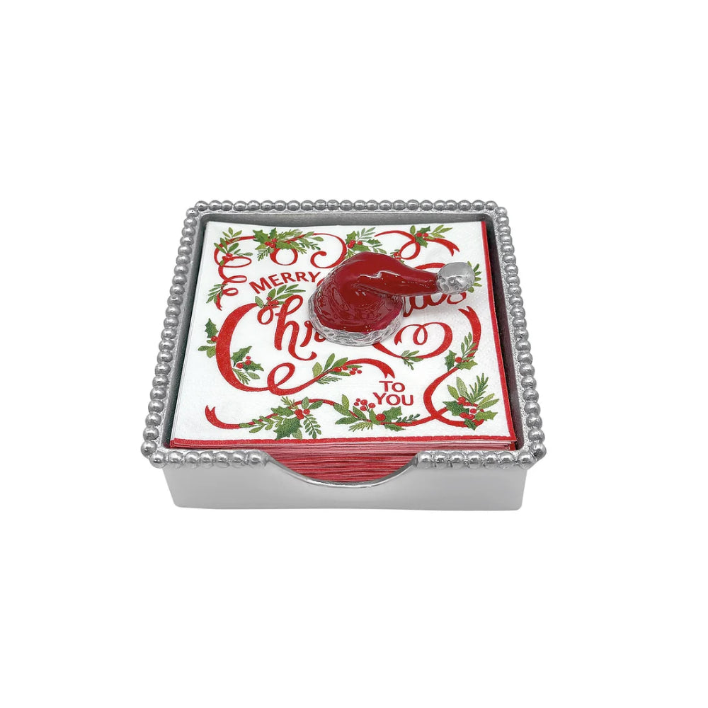 Red santa hat beaded napkin holder with white and red "Merry Christmas" napkins and santa hat weight on a white backround. 