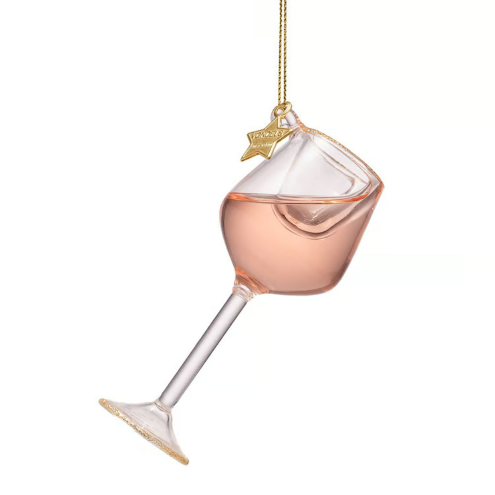 A clear glass wine glass ornament filled with pale pink liquid, hanging from a gold string with a small gold star topper, shown on a plain white background.