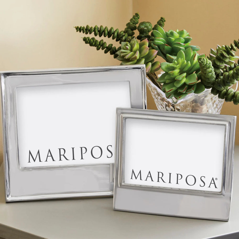 A 4x6 Rectangular metallic frame with a larger one on a grey table with clear vase with green plant with a tan painted wall in the backround.
