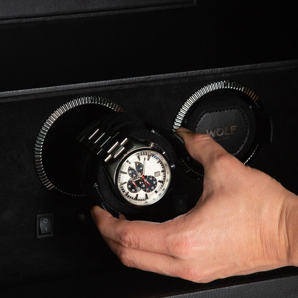 Hand holding a watch in a black display case with 'WOLF' branding.