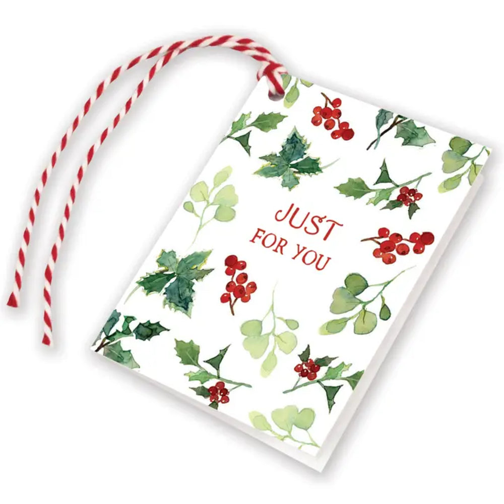 A white Christmas-themed gift tag with a red and white striped string, decorated with watercolor holly leaves and red berries, and featuring the text 'JUST FOR YOU' in red.