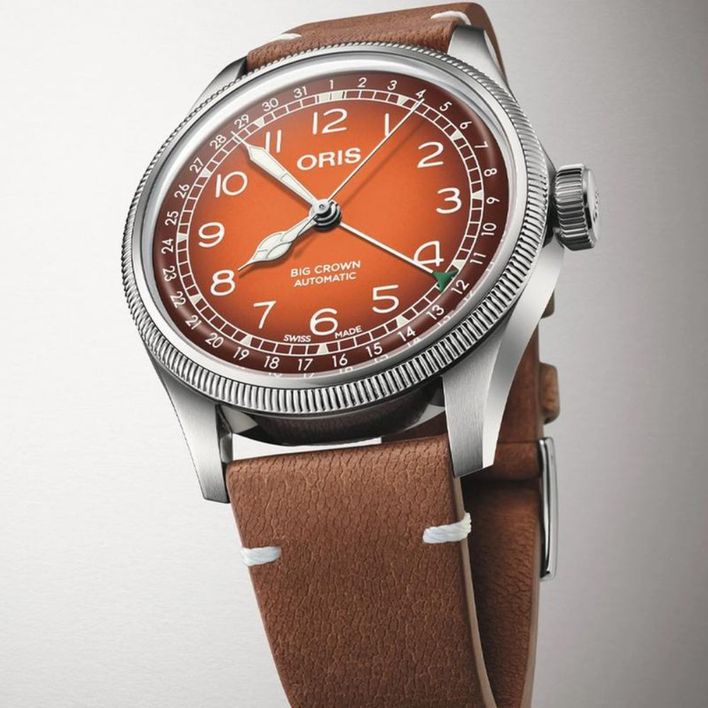 An Oris Swiss Crown Automatic watch featuring a brown leather strap, a silver stainless steel case, and a distinctive orange dial with white Arabic numerals.
