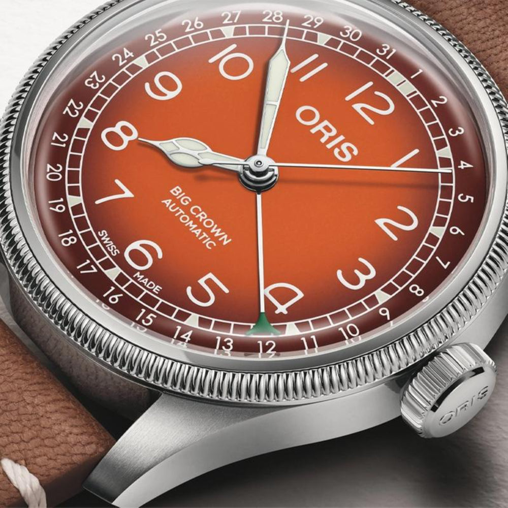 Close-up of an Oris Big Crown Automatic watch with a vibrant orange dial, silver stainless steel case, and a brown leather strap.