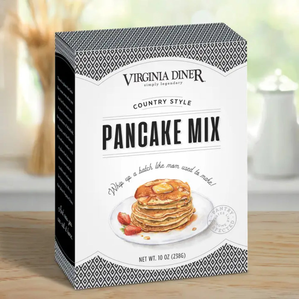 A box of Virginia Diner Country Style Pancake Mix, 10 oz, standing on a wooden surface with a softly blurred kitchen background.