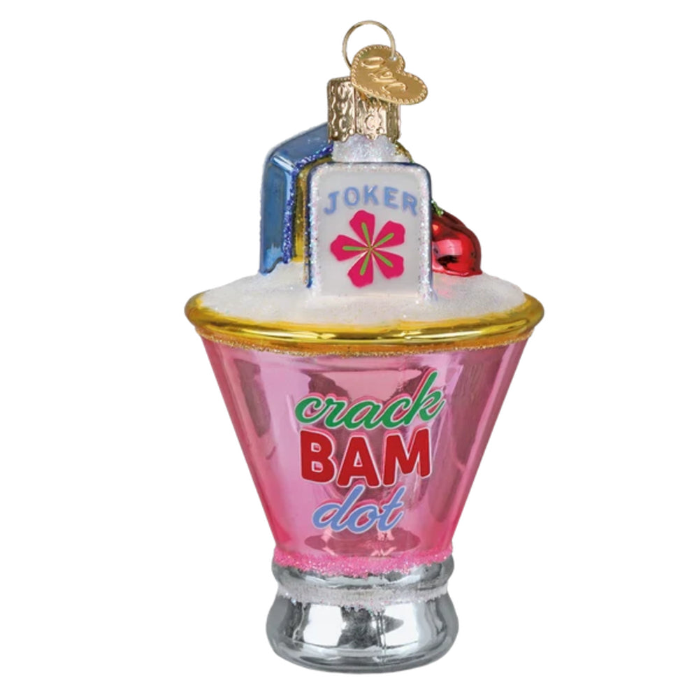 A novelty Christmas ornament shaped like a pink cocktail glass with the words 'crack BAM dot' on the front, topped with a white foam layer, a small blue card reading 'JOKER' with a pink flower, and a gold hanging loop, shown on a plain white background.