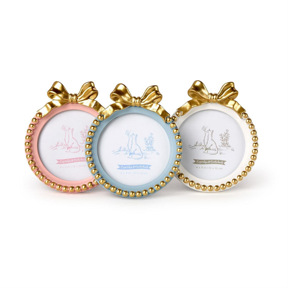 Three round decorative picture frames with bow tops and beaded borders, shown on a white background. The frames are pink, light blue, and white, each with a gold bow and gold beaded edge.