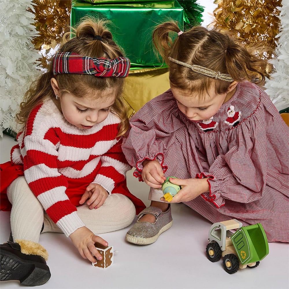 Two young girls playing with christmas themed toys in front of a Christmas tree.