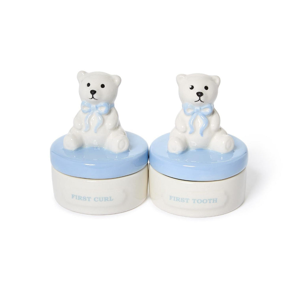 Two small ceramic keepsake jars shaped like white teddy bears sitting on light blue lids, with the words 'FIRST CURL' and 'FIRST TOOTH' printed on the front, shown on a white background.