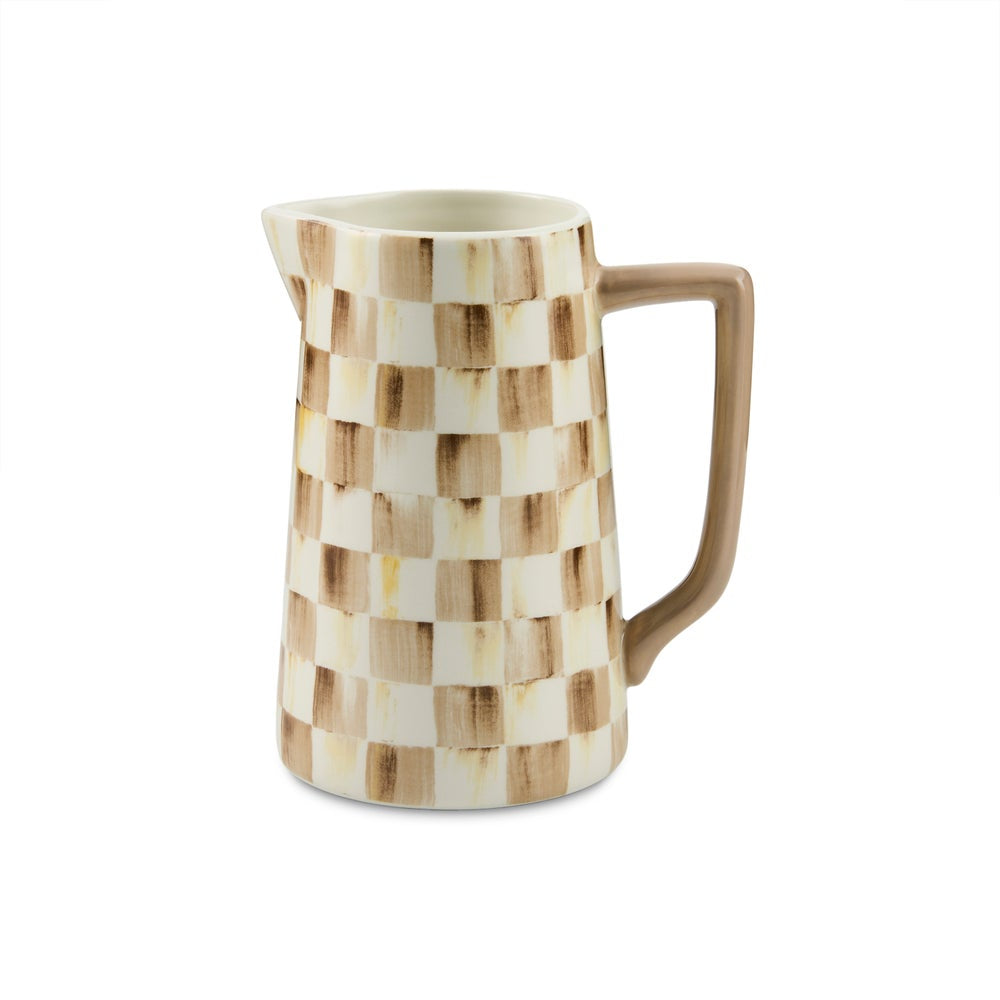 A ceramic pitcher with a woven checkered pattern in shades of brown and cream, featuring a solid brown handle and spout, set against a plain white background.