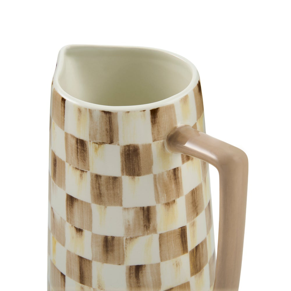 A close-up of a ceramic pitcher with a brown and cream checkerboard pattern and a smooth taupe handle, shown on a white background.