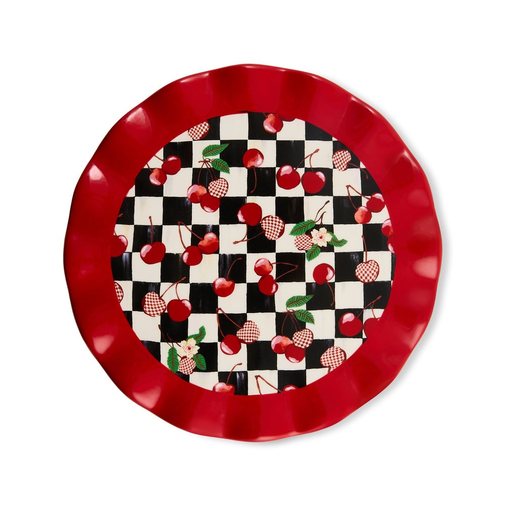 A round decorative serving platter with a scalloped red rim and a black-and-white checkerboard center pattern decorated with red cherries, green leaves, and small red-and-white checkered motifs, shown on a white background.