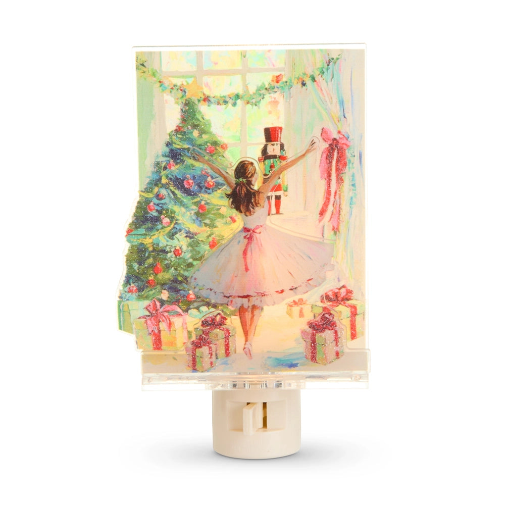 A Christmas-themed night light featuring a printed illustration of a ballerina in a pink tutu dancing beside a decorated Christmas tree, gift boxes, and a nutcracker, set in a clear acrylic frame on a cream-colored base.