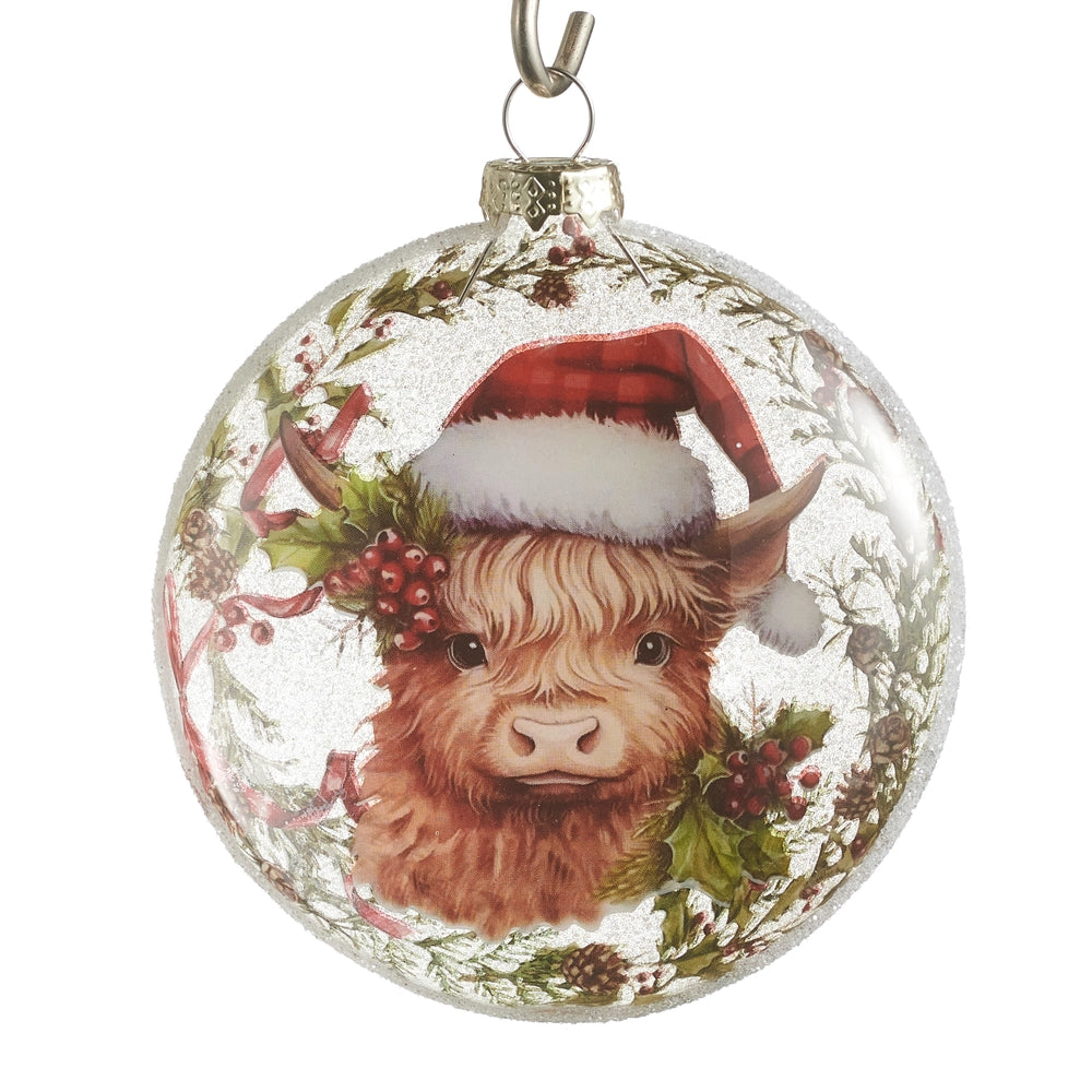 Christmas ornament with a highland cow wearing a Santa hat and surrounded by holly.