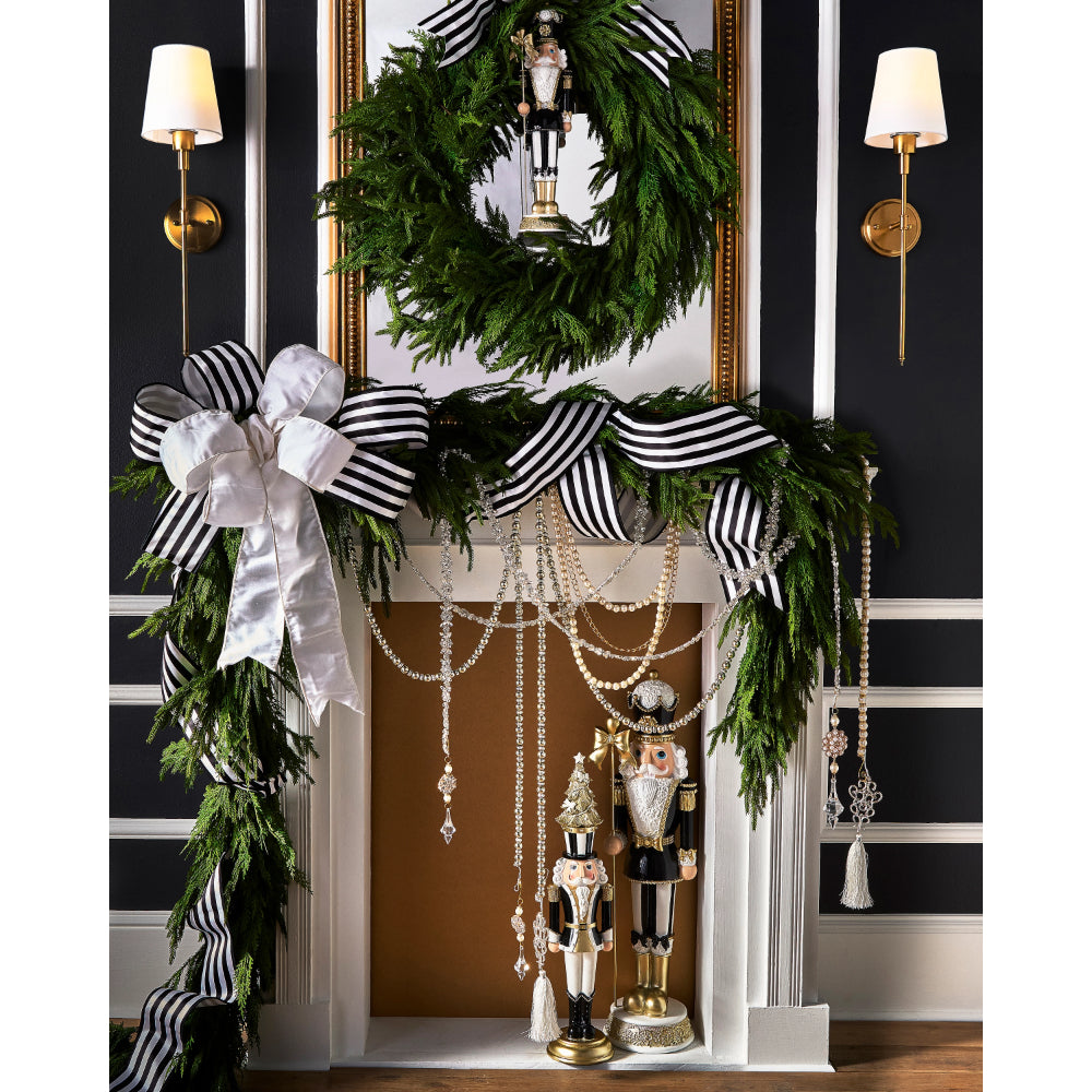 Decorative Christmas mantel with greenery, ribbons, and nutcrackers against a black wall.