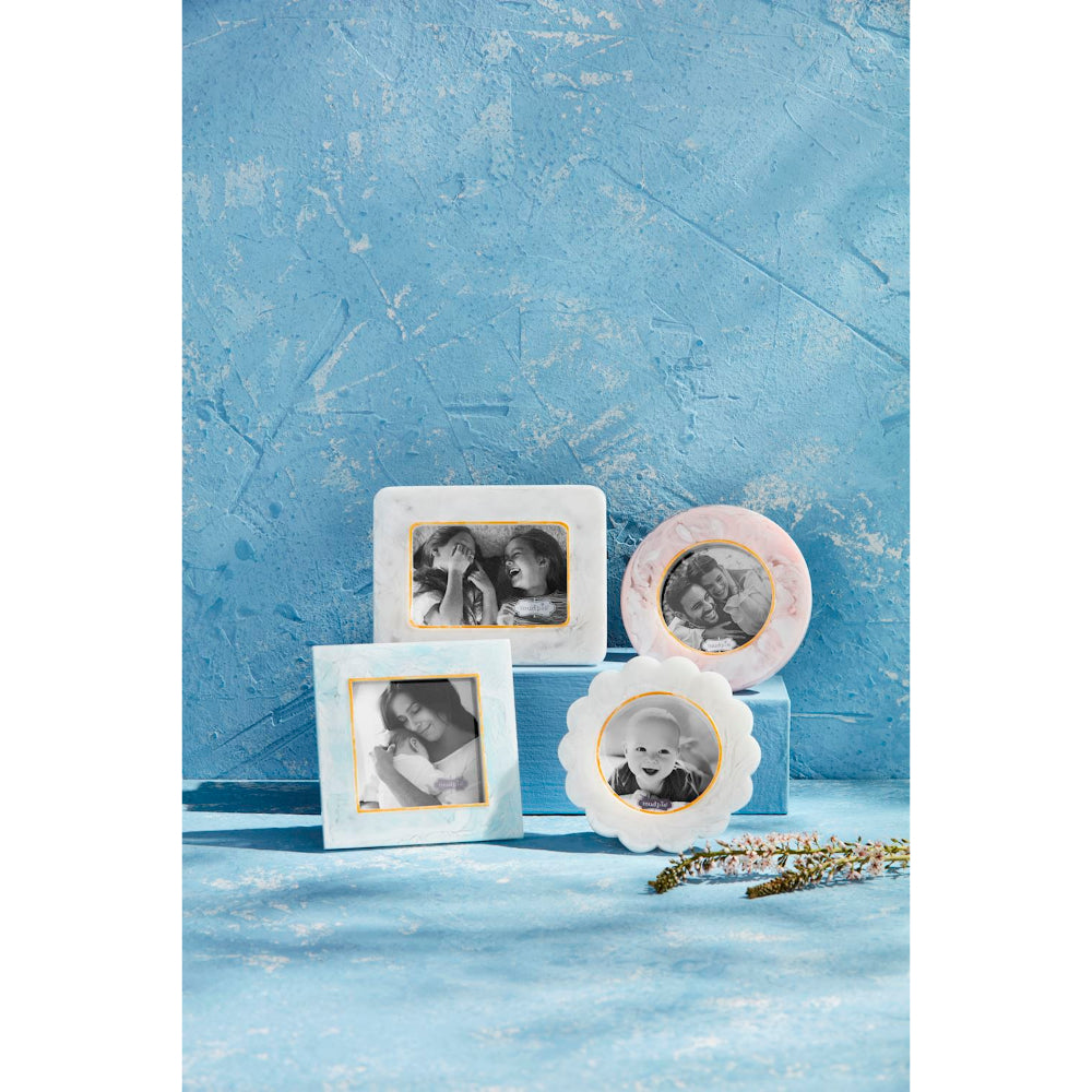 Four decorative picture frames in pastel blue, pink, and white with gold inner borders, displayed on a textured blue surface against a matching blue background. The frames are shown holding black-and-white photos of children.