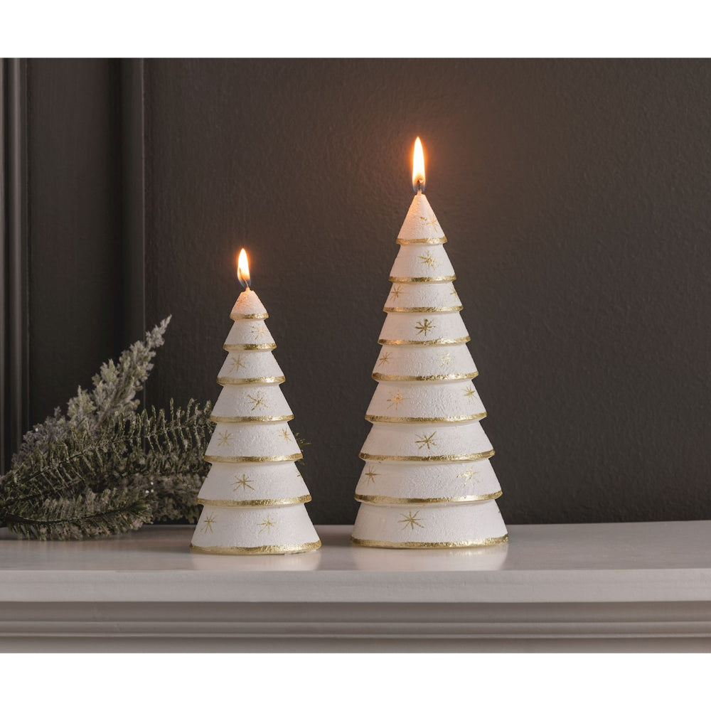 Two white Christmas tree-shaped candles with gold star details and gold trim, lit and displayed on a mantel against a dark background.