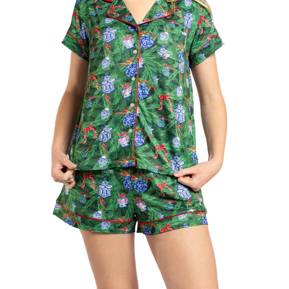 A model wearing a two-piece green pajama set with a Christmas tree and gift print, featuring red piping on the collar, placket, and shorts.
