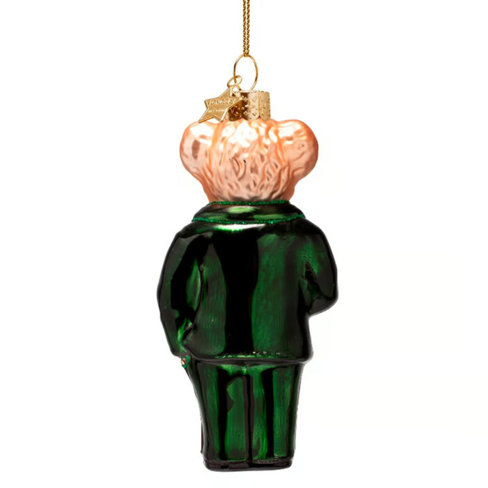 A glass Christmas ornament shaped like a bear wearing a dark green suit and a peach-colored fluffy hat, suspended by a gold string against a plain white background.