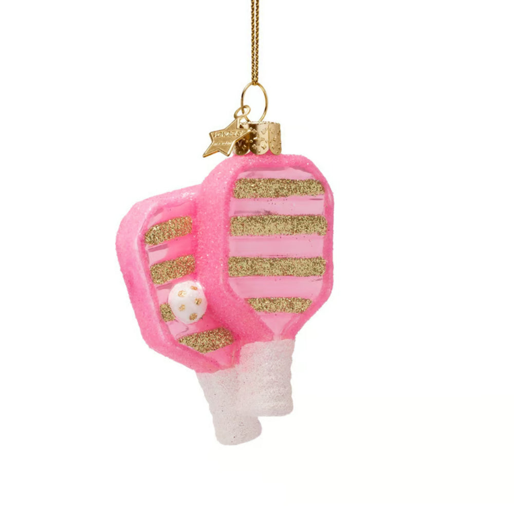 A pink and gold glitter Christmas ornament shaped like a pickleball paddle, with a small white ornament hanging from a gold string against a white background.