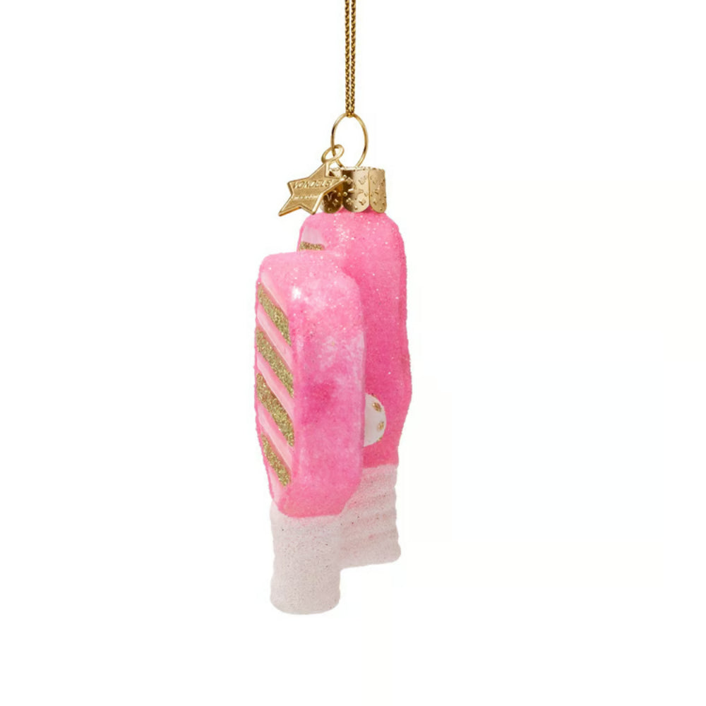 A pink and white glittery ornament shaped like a pair of pickleball paddles with gold glitter stripes and a gold hanging loop, shown against a plain white background.