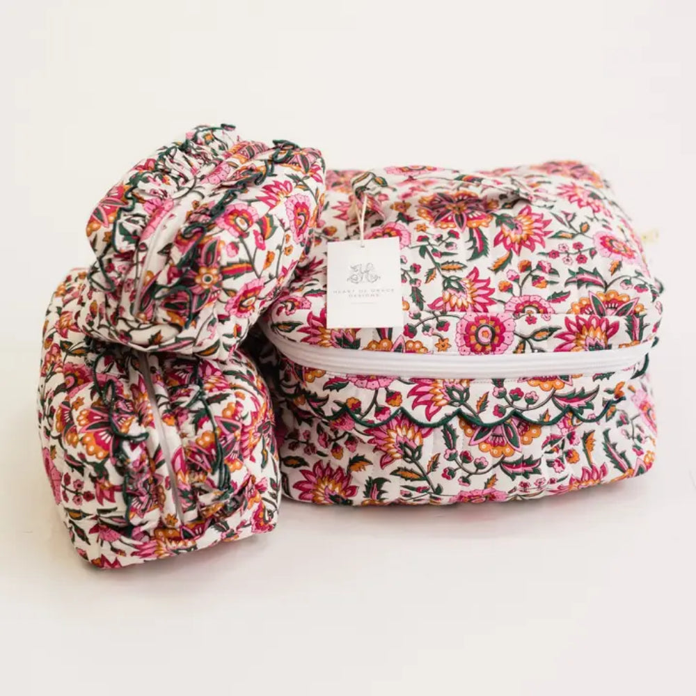 A floral-patterned fabric storage bag with a white zipper, shown next to two matching rolled fabric pouches. The fabric features a dense multicolor print of pink, orange, red, green, and yellow flowers on a white background.