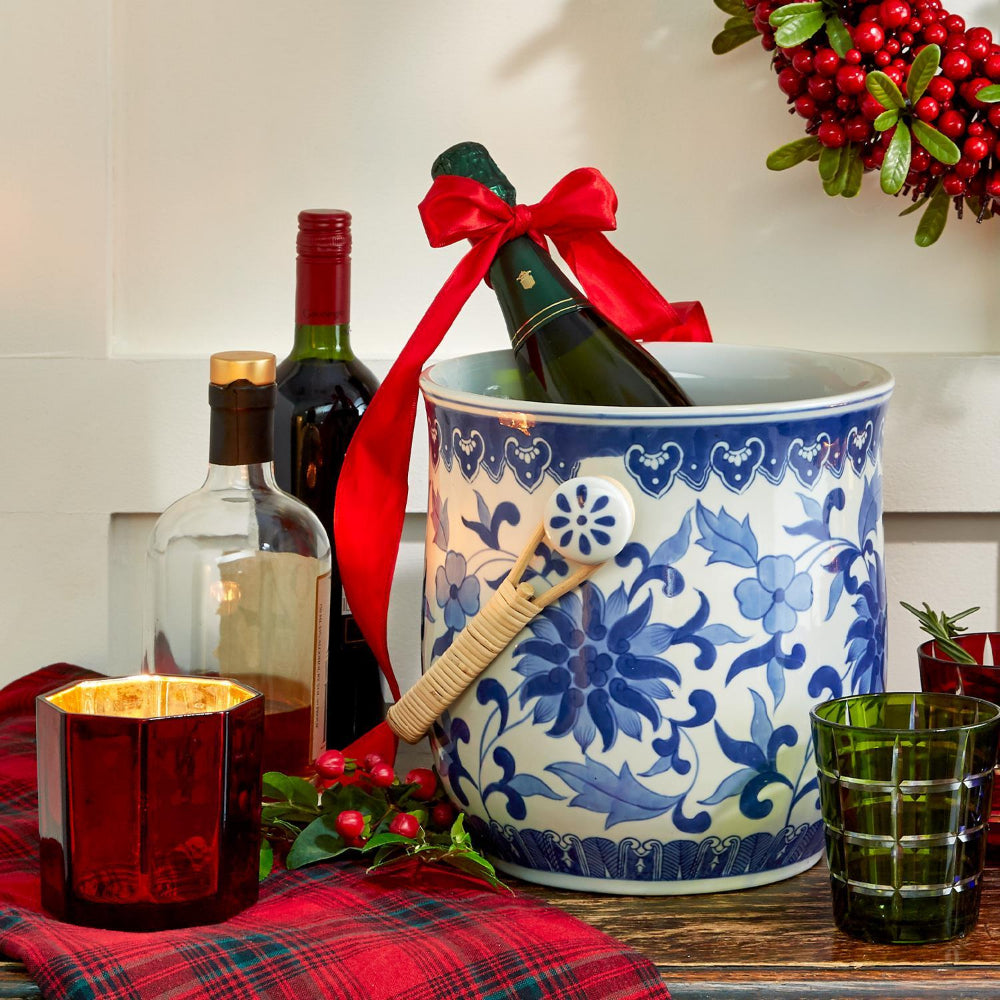 Decorative wine cooler with a bottle of wine, glasses, and candles on a table with a festive wreath in the background.