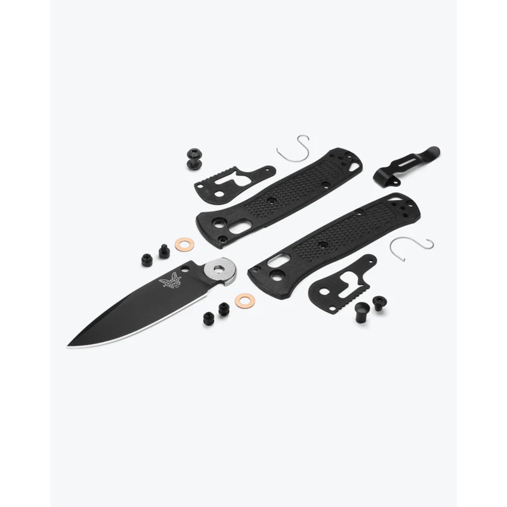 A black folding knife shown disassembled with all of its components laid out on a light gray background. The kit includes the black blade, two textured black handle scales, a silver bolster, screws, washers, and small metal hooks.