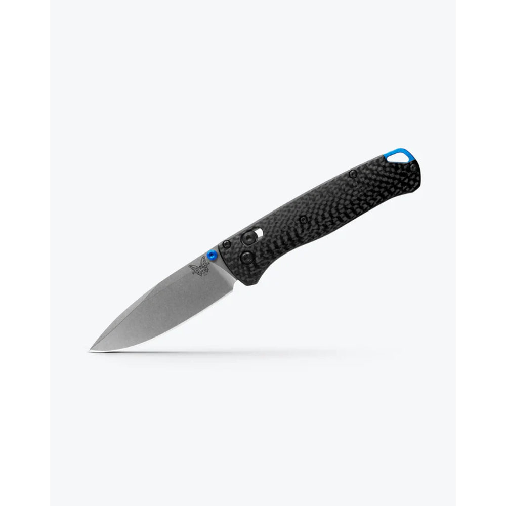 A folding pocket knife with a textured black carbon fiber handle and a silver steel blade, featuring small blue accents near the bolster and handle end, shown against a light gray background.