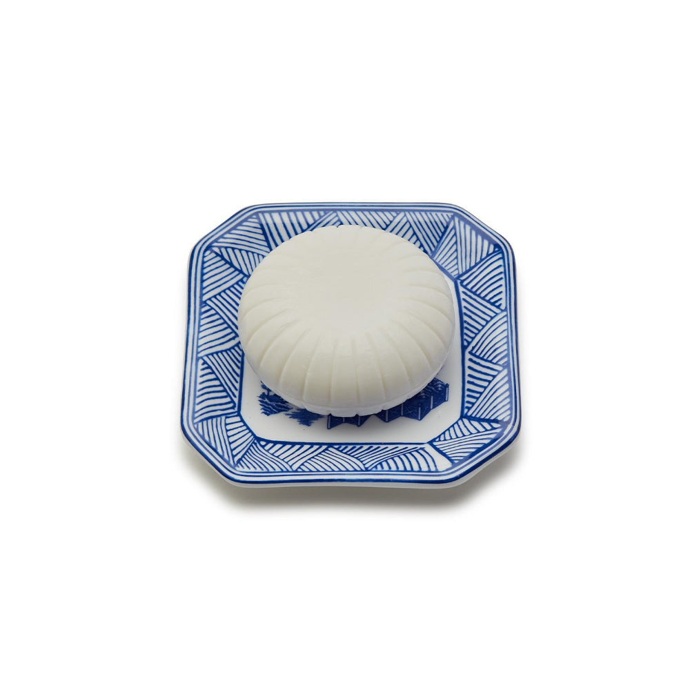 A round, blue and white porcelain tray with a soap bar embossed with a floral design on a white backround. 