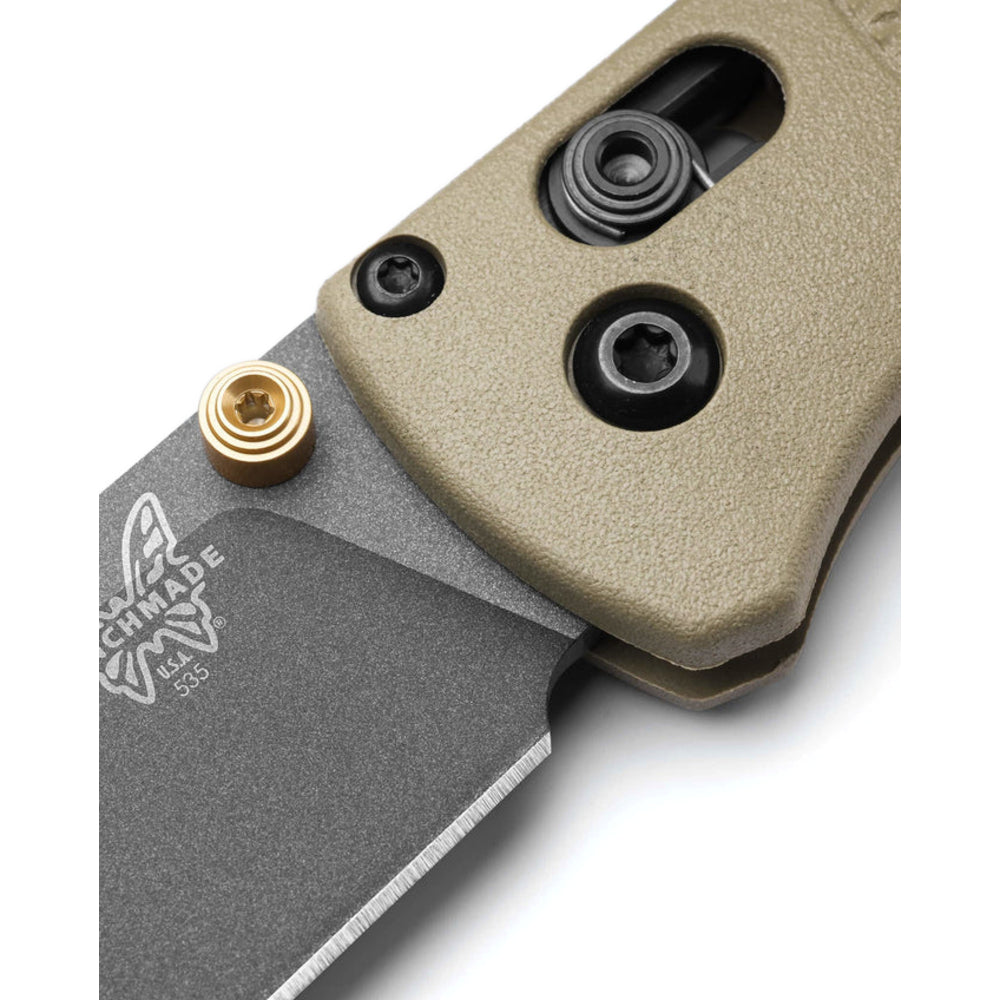 Close-up of a folding knife showing a textured tan handle, a dark gray steel blade, a brass accent screw, and black screws on a white background.