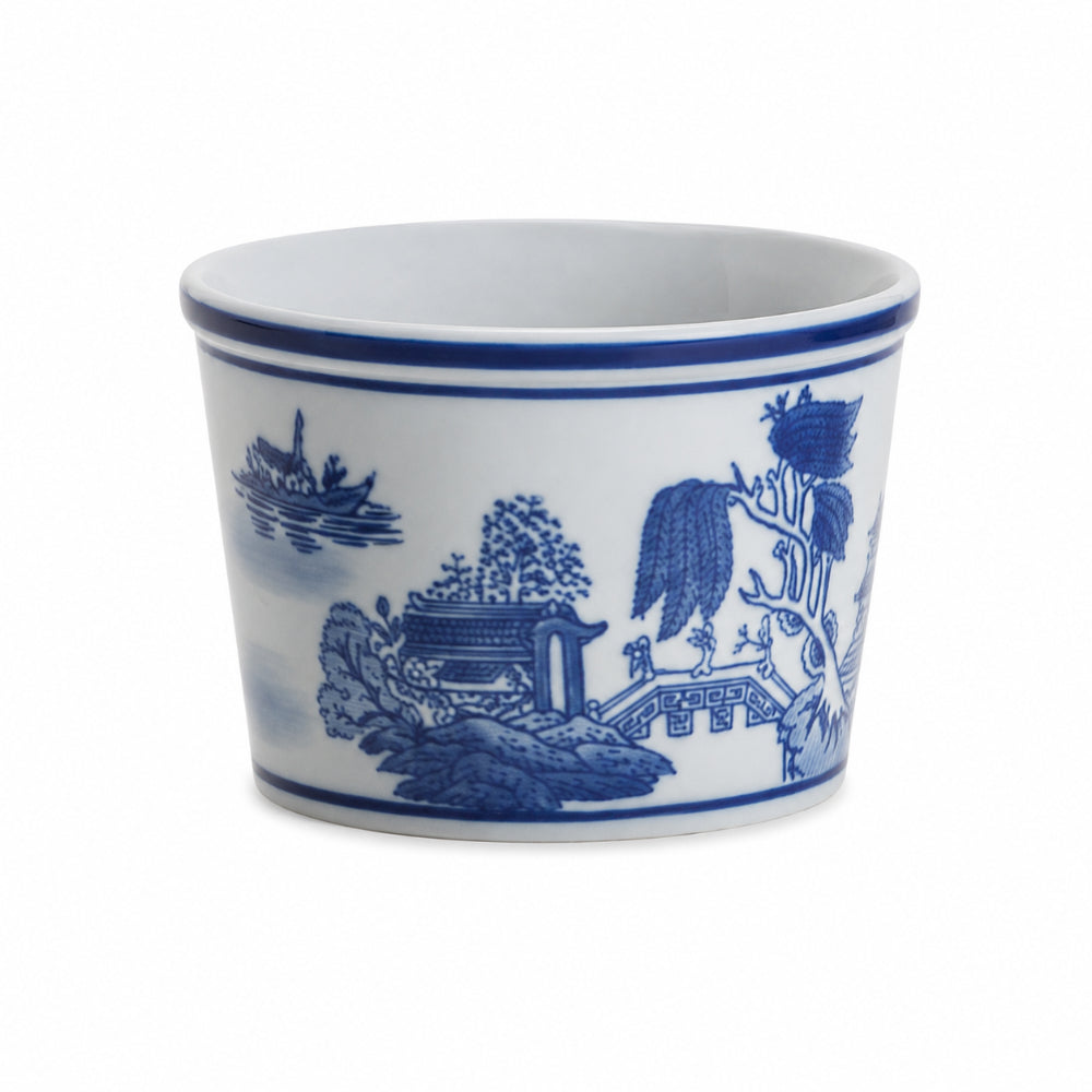 A white ceramic cup decorated with a classic blue and white Chinese landscape pattern featuring trees, a pagoda, and a bridge.