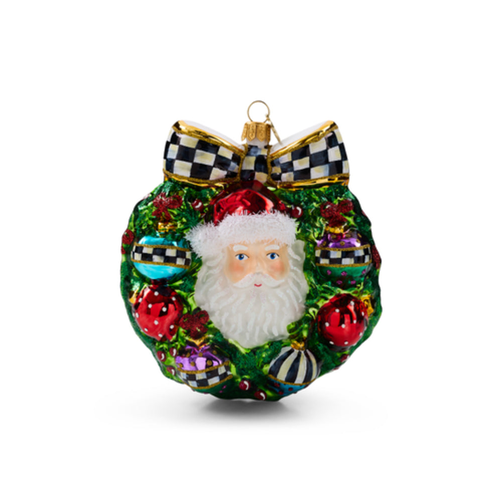A Christmas ornament shaped like a green wreath with a white Santa face in the center, red and striped ornaments, and a black-and-white checkered bow at the top, shown on a plain white background.