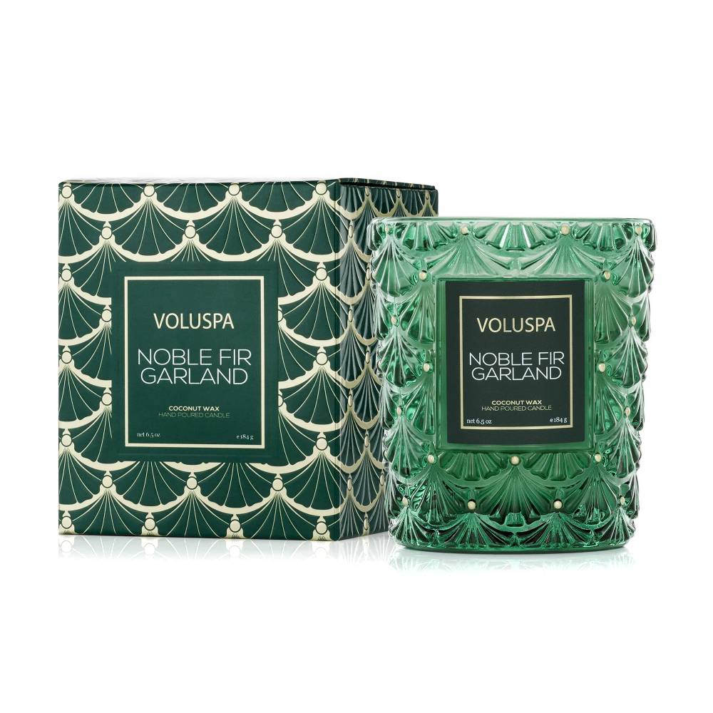 A VOLUSPA Noble Fir Garland coconut wax candle in a green patterned glass jar next to its matching green and gold patterned box, on a white background.