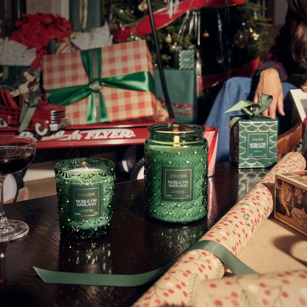 Green candles on a table with festive decorations in the background.