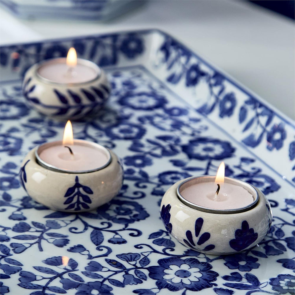 Three lit candles in decorative ceramic holders on a blue and white patterned tray.