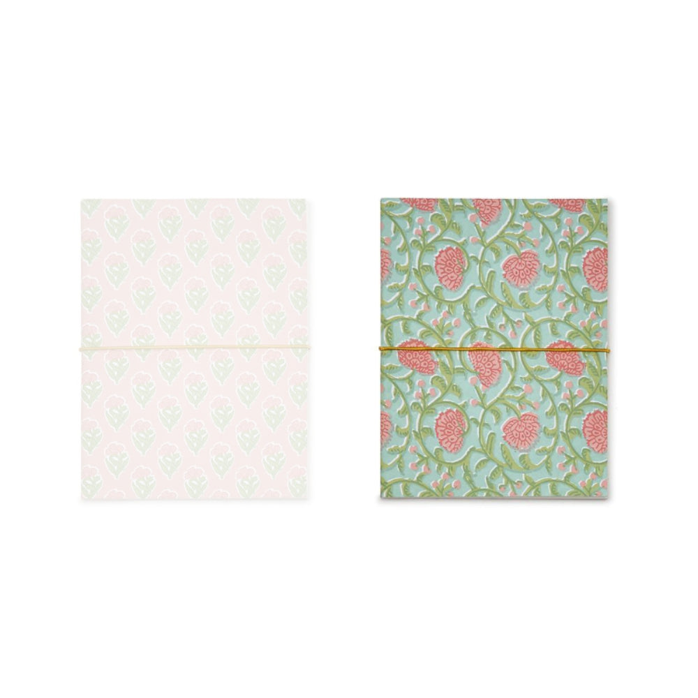 A green paper back notebook with a green floral pattern with pink berry accents on a white backround. 