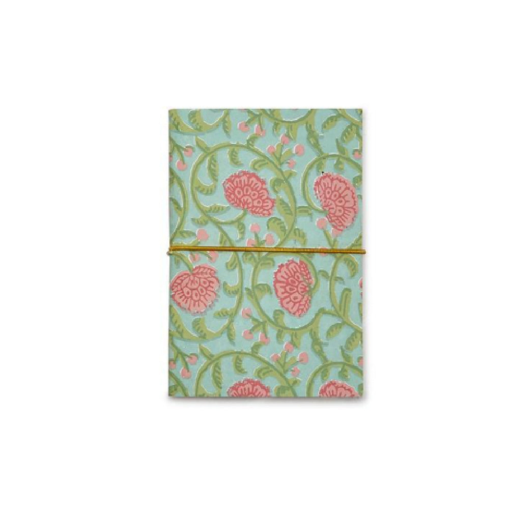 A folded notebook or journal with a light blue-green background, decorated with a pink floral and green vine pattern, held closed by a thin gold elastic band.