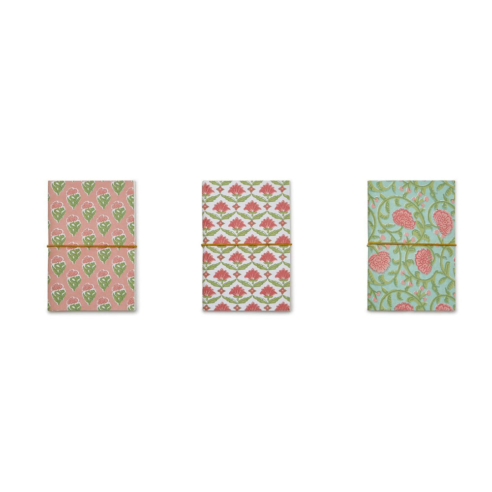 Three small patterned notebooks or journals tied with thin gold bands, arranged side by side on a plain white background. The left notebook has a pink and green floral pattern, the middle has a red and green geometric floral pattern, and the right has a mint green and pink floral pattern.