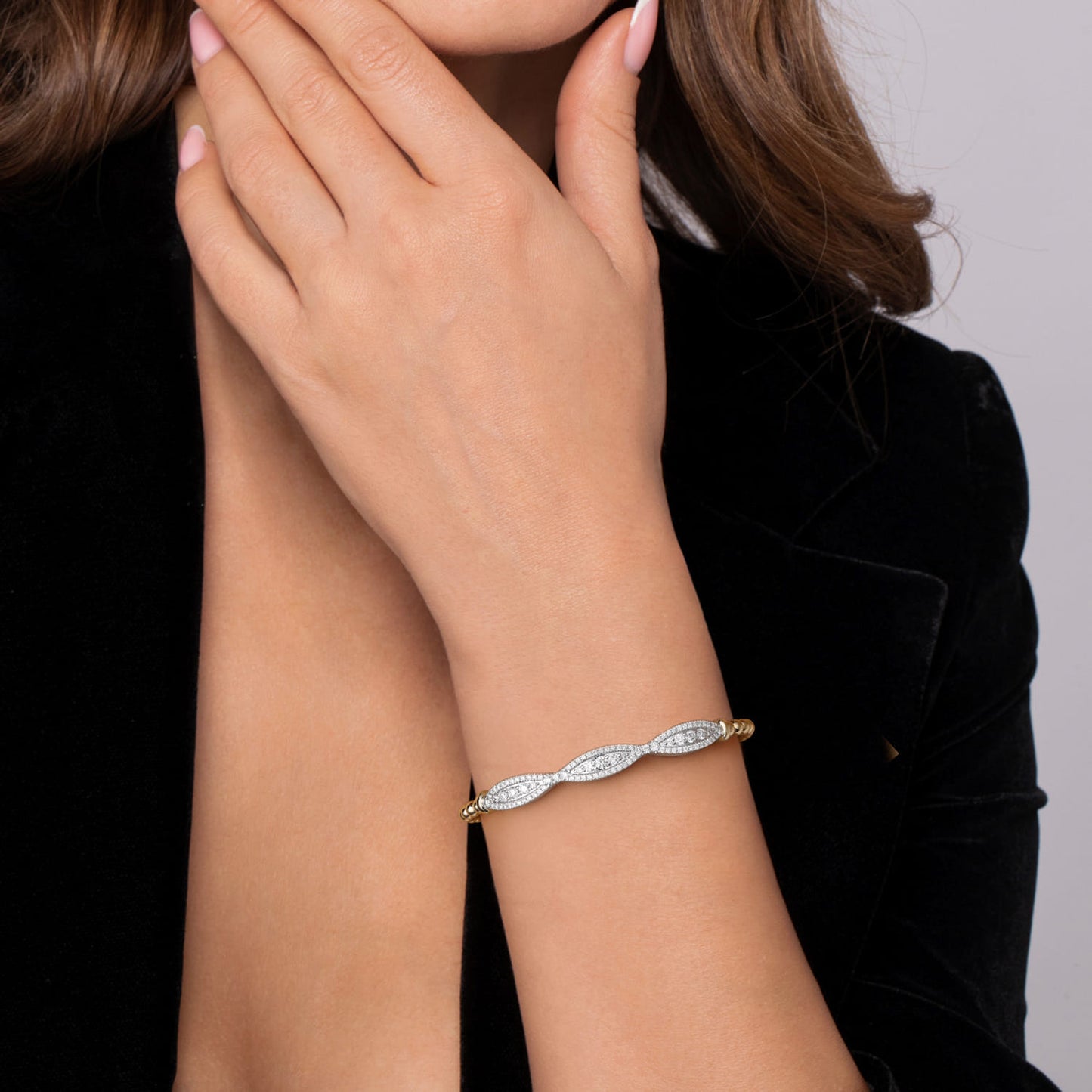 A close-up of a woman's wrist wearing a delicate silver-toned bracelet with pavé-set clear stones and small rose gold end accents, paired with a black velvet jacket.