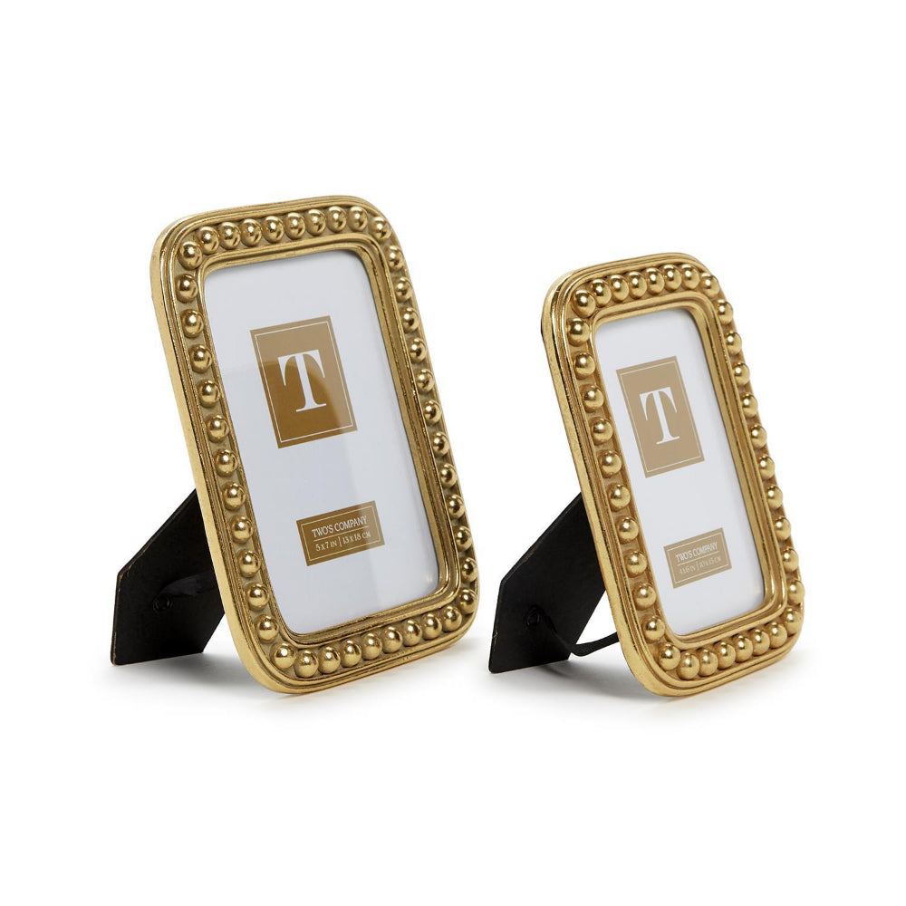 Two gold picture frames with beaded borders in sizes 4x6 and 5x7 with black easel stands, shown on a white background. Each frame has a placeholder insert with a gold square and the letter T.