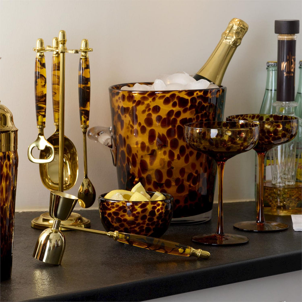 Tortoise shell  print ice bucket with champagne bottle, glasses, and bar tools on a dark surface.
